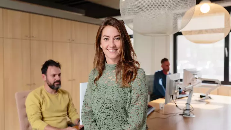 Een collega kijkt richting de camera terwijl de rest van het team op de achtergrond verder aan het vergaderen is