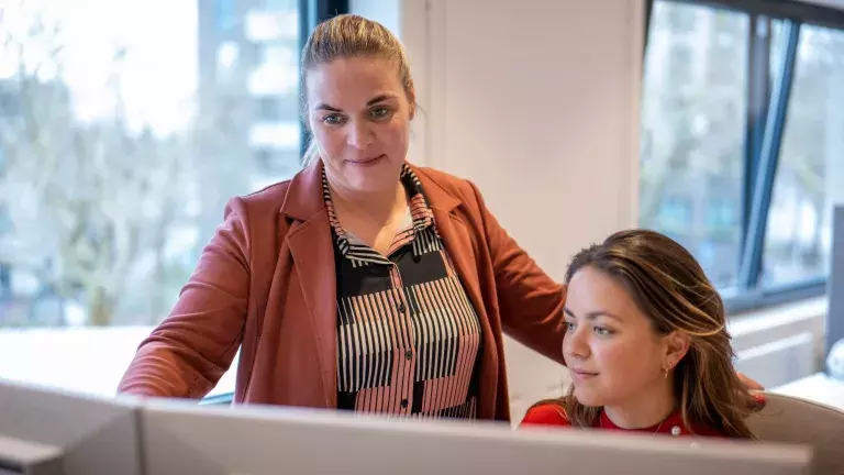 Liesbeth van Kerkwijk geeft instructies aan een collega achter een computer